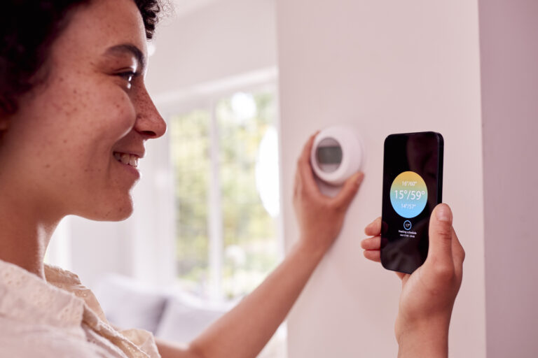 Close Up Of Woman Using App On Mobile Phone To Control Central Heating Thermostat At Home